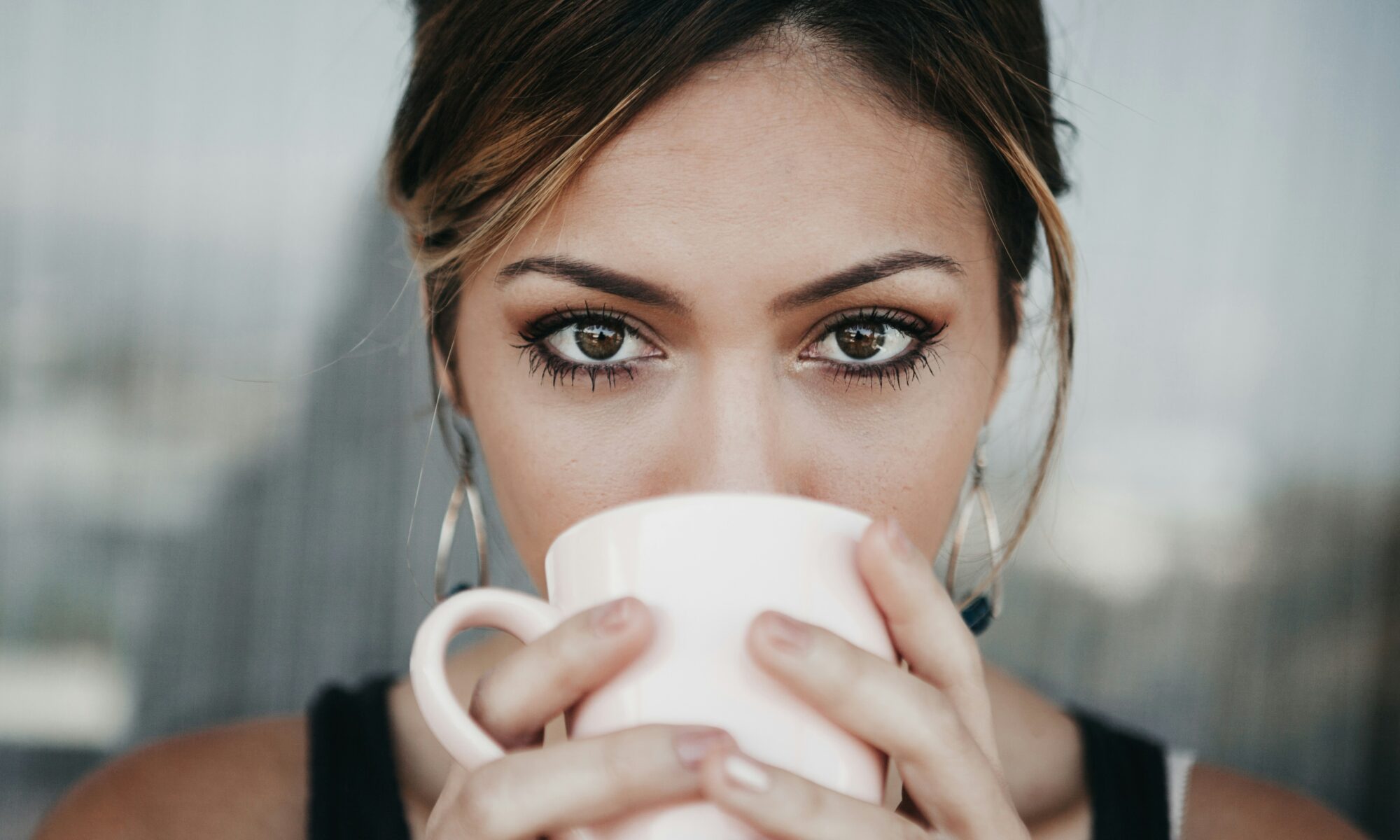 woman holding a coffee cup in front of her lips and looking at the camera