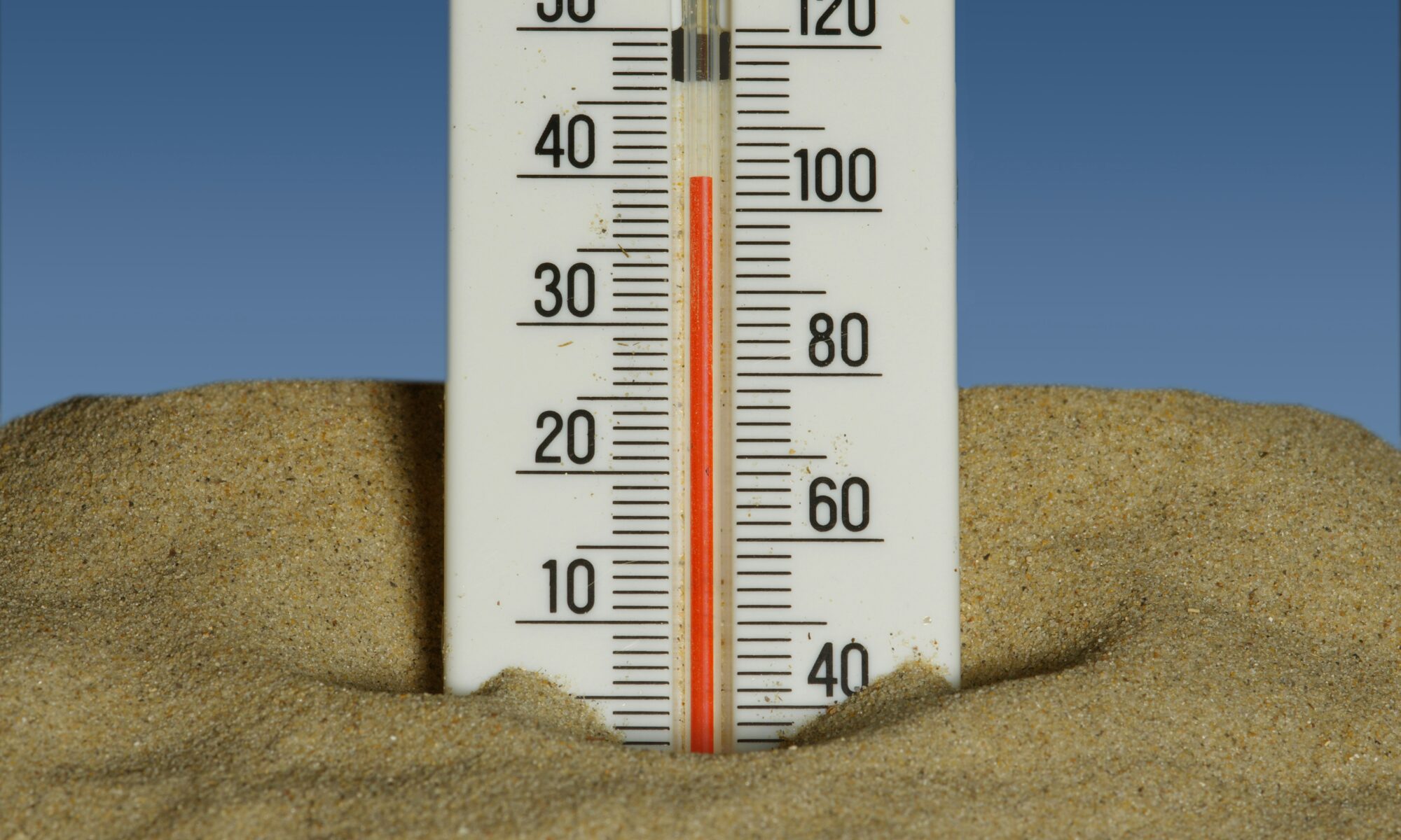 a thermometer in the sand with a blue sky background