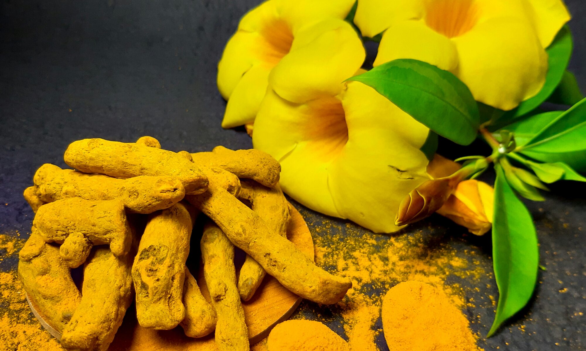 turmeric spice ground and whole next to yellow flowers